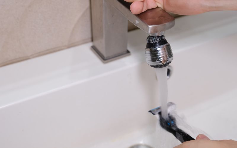 Hand rinsing razor under running faucet in bathroom sink