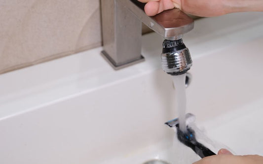 Hand rinsing razor under running faucet in bathroom sink