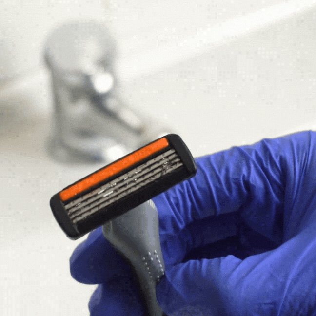 Razor being sprayed with cleaning spray over a sink